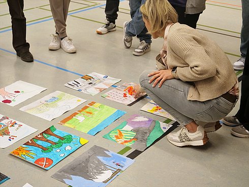 Eine Frau hockt auf dem Boden, vor ihr liegen in Viererreihen übereinander gemalte Bilder.