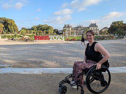 Eine Frau im Rollstuhl, im Hintergrund der Schriftzug "Paris 2024".